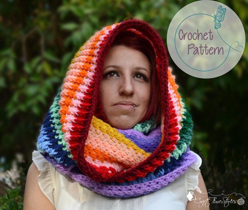 May include: A colorful rainbow crochet hooded scarf with a purple, blue, green, yellow, orange, and red color pattern. The scarf is worn by a person with red hair.