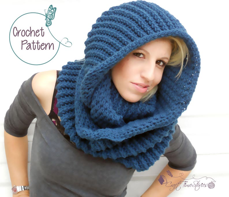 May include: A blue crocheted cowl with a hood. The cowl is worn by a person with blonde hair. The cowl is made with a textured stitch.