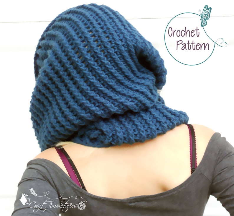 May include: A blue crocheted cowl or hood with a ribbed texture. The cowl is worn by a person with a gray shirt. The text "Crochet Pattern" is visible in the image.