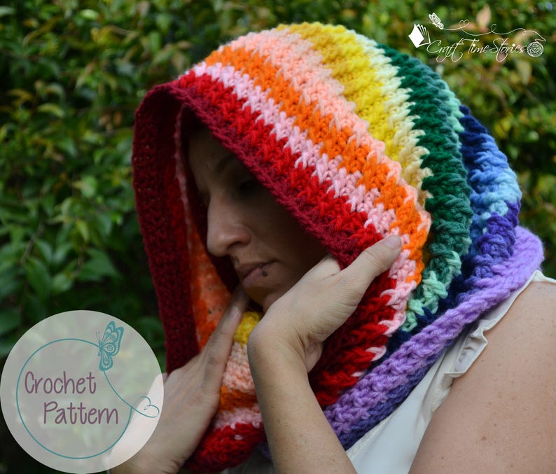 May include: A rainbow crochet hooded cowl with a textured stitch pattern. The cowl is made with a variety of colors, including red, orange, yellow, green, blue, and purple.