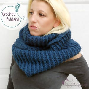 May include: A close-up of a woman wearing a blue crocheted cowl neck scarf. The scarf is thick and textured, and the woman is wearing a black shirt. The text "Crochet Pattern" is visible in the image.