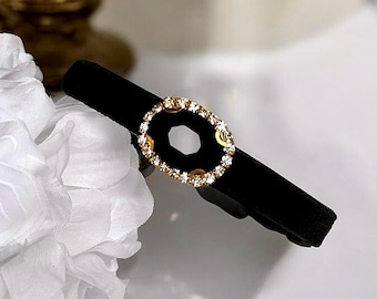 Könnte beinhalten: Ein schwarzes Samt-Haarband mit einem goldfarbenen, ovalen Strass-Schmuckstück.