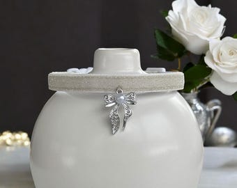 May include: A white ceramic jar with a silver glitter ribbon and a silver bow charm with a pearl in the center.