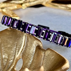 Peut inclure: Un collier pour animal de compagnie orné de pierres rectangulaires violettes et argentées. Le collier est sur un fond doré.