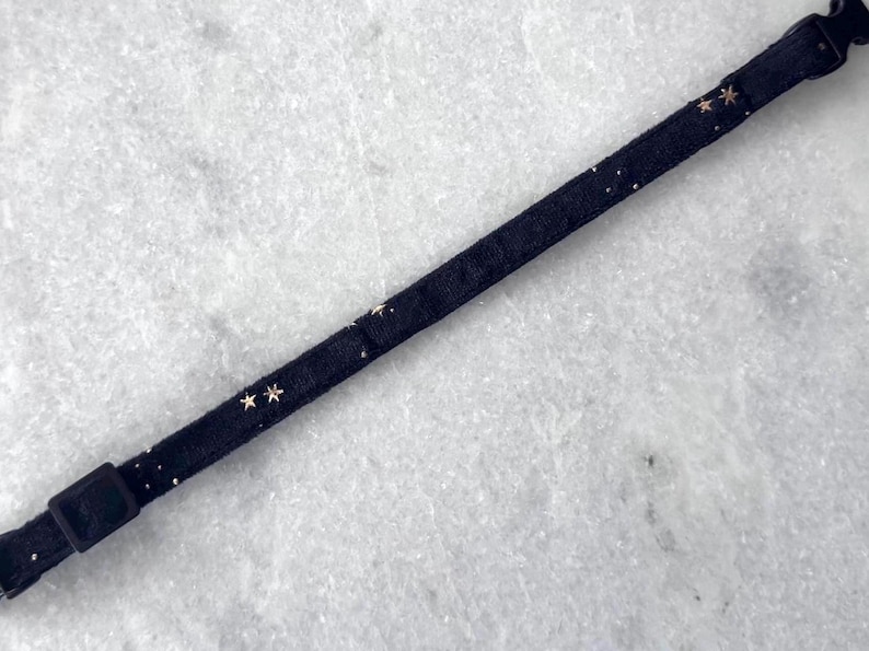 Puede incluir: Un collar negro ajustable con detalles de estrellas doradas. El collar est&aacute; hecho de una tela suave y c&oacute;moda.