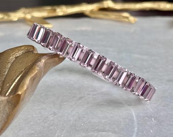May include: A pink crystal bracelet with rectangular shaped stones. The bracelet is made of clear metal and has a delicate design.