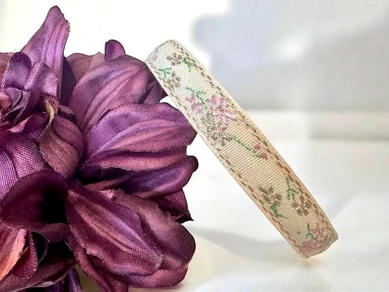 K&ouml;nnte beinhalten: Ein beigefarbenes Band mit einem floralen Muster in Rosa und Gr&uuml;n. Das Band ist gerollt und hat einen gen&auml;hten Rand.