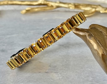 Puede incluir: Un collar de tono dorado con un diseño de cadena que presenta piedras rectangulares facetadas de color ámbar.