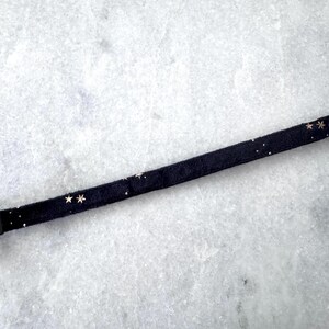 Puede incluir: Un collar de tela negro con detalles de estrellas doradas.
