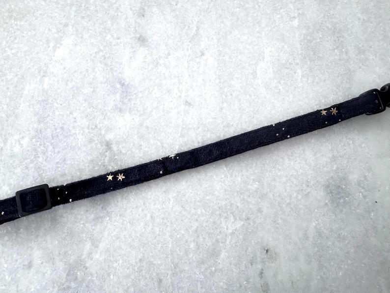 Puede incluir: Un collar de tela negro con detalles de estrellas doradas.