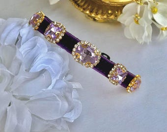 May include: A purple velvet choker with five large, clear, faceted, square-shaped rhinestones. The rhinestones have a light purple hue.