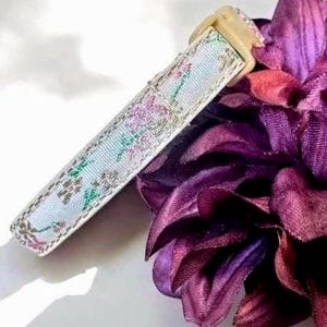 K&ouml;nnte beinhalten: Ein hellblaues und wei&szlig;es Hundehalsband mit floralem Muster und einer beigefarbenen Kunststoffschnalle.