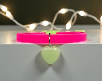 Könnte beinhalten: Ein leuchtend neonpinkes Haustierhalsband mit einer hellgrünen Kunststoffschnalle und einem baumelnden herzförmigen Anhänger in blassem, durchscheinendem Mintgrün. Das Halsband besteht aus einem glatten, flexiblen Material und hat einen Metallring.