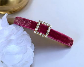 May include: A pink velvet headband with a gold square-shaped rhinestone buckle.