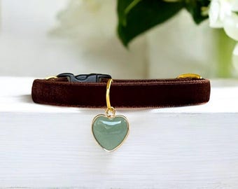 Pode incluir: Uma coleira de veludo castanho escuro com um anel de metal dourado e um pendente em forma de coração com uma pedra lisa verde clara. A coleira inclui uma fivela de plástico preta e um ajustador deslizante de metal dourado.