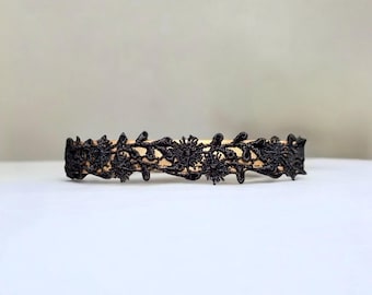 May include: Black lace trim with a floral design. The trim is on a beige background.