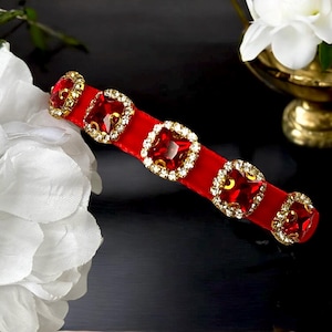 May include: Red velvet headband with gold-toned embellishments and red square-shaped rhinestones.