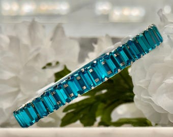 Puede incluir: Un brazalete azul turquesa con piedras de imitación rectangulares engastadas en una banda de metal plateado.