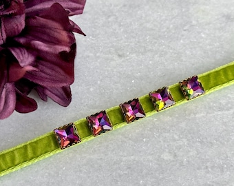 Puede incluir: Un collar gargantilla de terciopelo verde con cinco piedras de cristal cuadradas iridiscentes.