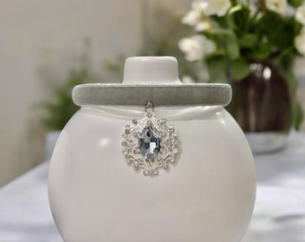 May include: A gray velvet choker with a silver pendant featuring a clear rhinestone in the center. The pendant is a delicate, ornate design.