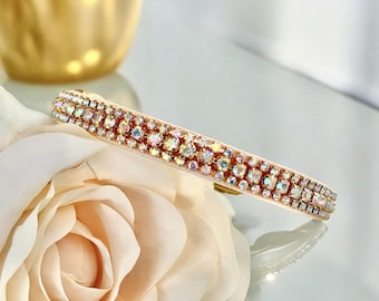 May include: A sparkling hair barrette with iridescent rhinestones. The barrette is rectangular and features a light pink base. The rhinestones are arranged in rows, creating a dazzling effect. The barrette is placed on a cream-colored rose.