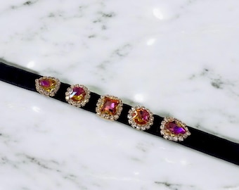 May include: A black velvet choker necklace with five gold-toned settings, each featuring a pink and yellow iridescent gemstone. The gemstones are surrounded by smaller clear rhinestones.