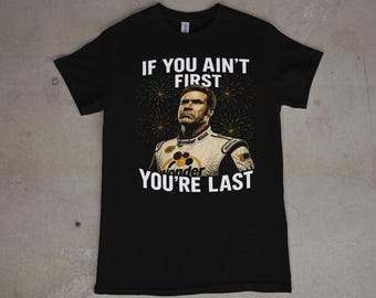 May include: Black t-shirt with the quote "IF YOU AIN'T FIRST YOU'RE LAST" in white text, featuring an image of a man in a racing suit. The image includes fireworks in the background. The shirt is made of a soft material.