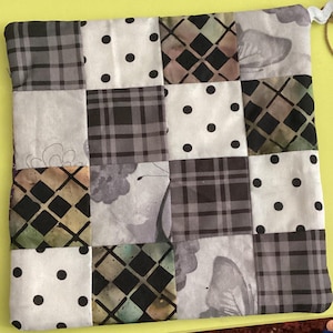 Puede incluir: Una bolsa de tela de patchwork con una variedad de patrones, incluyendo cuadros, lunares y diseños florales. La bolsa tiene un cordón blanco y una etiqueta marrón.