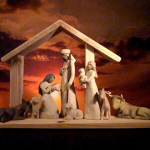 May include: A wooden nativity scene depicting the holy family, animals, and a shelter. The figures are carved in a simple style and painted in neutral tones. The background is a sunset with orange and red hues.