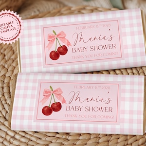 Può includere: Due barrette di cioccolato con involucri a quadretti rosa. Ogni involucro presenta un'etichetta rosa con ciliegie, un fiocco e il testo "Maria's Baby Shower". Sono inclusi anche i testi "February 8th 2028" e "Thank you for coming!"