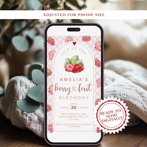 May include: A smartphone displays a digital invitation for Amelia's first birthday. The invitation features a strawberry theme with the text "berry & first birthday." The design includes strawberries, leaves, and a pink gingham pattern. The invitation is ready to send digitally.