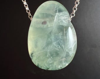 May include: A teardrop-shaped pendant made of a translucent, pale green stone with internal veining and inclusions, suspended from a silver-toned metal rolo chain. The stone features a smooth, polished surface with visible natural mineral patterns.