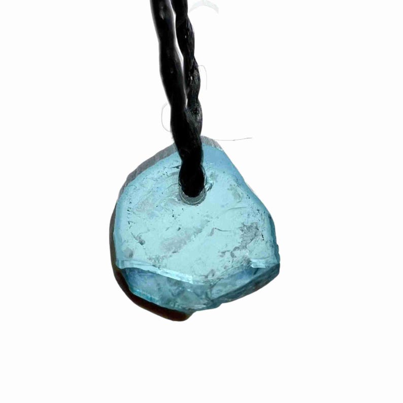 Pu&ograve; includere: Un ciondolo azzurro, di forma irregolare, con un foro nella parte superiore, sospeso a un cordino nero. Il ciondolo ha un aspetto leggermente traslucido e una superficie strutturata, suggerendo che possa essere fatto di vetro o materiale simile.