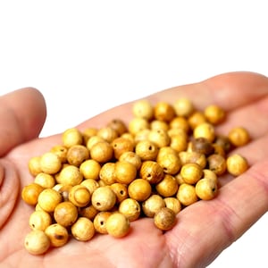 Può includere: Una mano che tiene un mucchio di perline di legno color marrone chiaro. Le perline sono lisce e rotonde, e hanno una venatura di legno naturale.