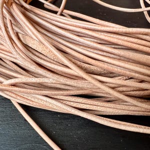 Könnte beinhalten: Nahaufnahme eines Bündels hellbrauner Lederschnüre. Die Schnüre sind eng gepackt, mit sichtbarer Textur und Farbvariationen. Das Leder scheint natürlich und unbehandelt zu sein, mit matter Oberfläche. Die Schnüre werden wahrscheinlich für Bastelarbeiten oder Schmuckherstellung verwendet.