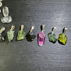 Può includere: Sette ciondoli in pietra preziosa di diversi colori su catene d'argento. I ciondoli sono tutti tagliati grezzi e hanno un aspetto naturale e grezzo. I colori includono nero, verde, rosa e giallo.