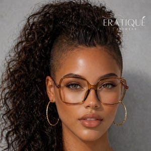 May include: A woman wearing large, brown-framed eyeglasses and gold hoop earrings. Her dark hair is styled in a high ponytail with a shaved side. The glasses have a square shape. The brand name "ERATIQUE EYEWEAR" is visible.