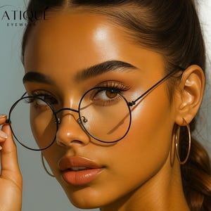 May include: Close-up of a person wearing round, black-rimmed eyeglasses. The glasses have a thin frame and are held near the face. The image also shows gold hoop earrings and the text "ERATIQUE EYEWEAR" in the upper left corner.