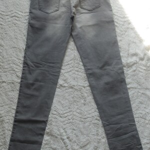 May include: A pair of gray denim jeans, laid flat, showcasing the back pockets and waistband. The jeans have a classic five-pocket design and a faded appearance. The fabric appears to be a medium-weight denim.