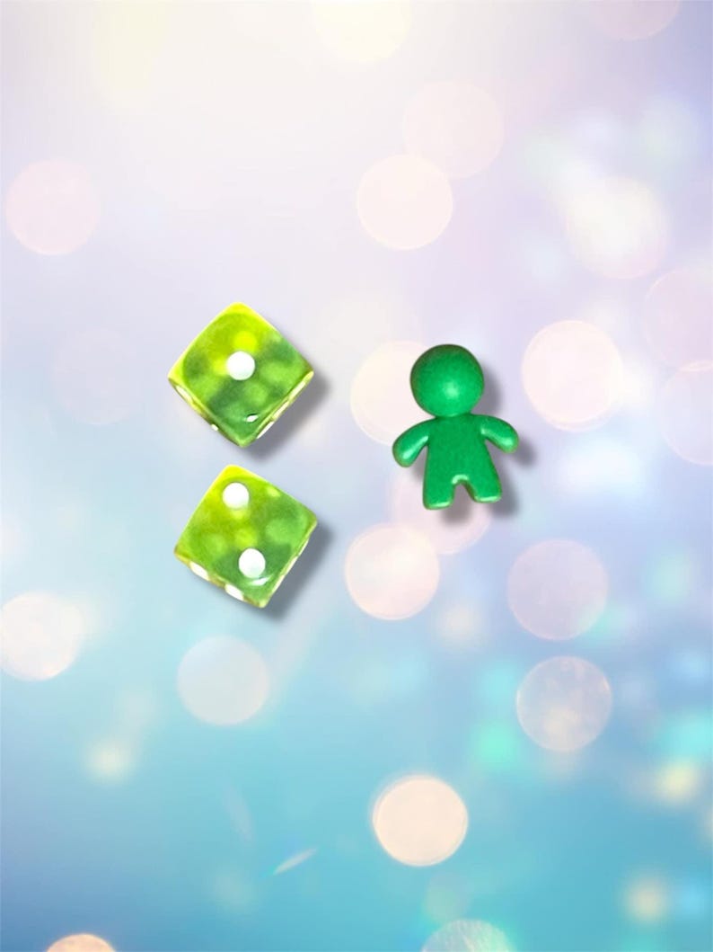 K&ouml;nnte beinhalten: Zwei gr&uuml;ne W&uuml;rfel mit wei&szlig;en Punkten und eine gr&uuml;ne Figur auf einem hellblauen Hintergrund mit wei&szlig;en und rosa Bokeh.