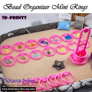 May include: Pink 3D printed bead organiser with numbered rings for storing beads. The organiser is filled with small colourful beads. The text "Bead Organizer Mini Rings" and "3D-PRINTS" is visible at the top of the image. The text "DiMarca Online" and "PATTERNS SEED BEADS CRYSTALS" is visible at the bottom of the image.