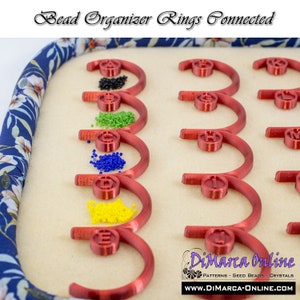 May include: Red plastic bead organizer rings connected together. Each ring is labeled with a letter from A to J.  Beads in various colors are displayed in front of each ring. DiMarca Online is printed on the bottom right corner of the image.