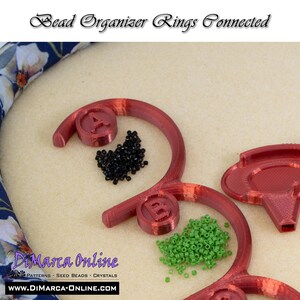May include: Red plastic bead organizer rings connected together. The rings are labeled A and B. Black and green seed beads are in the rings.