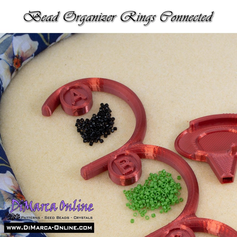 May include: Red plastic bead organizer rings connected together. The rings are labeled A and B. Black and green seed beads are in the rings.