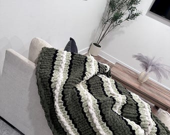 May include: A green, white, and black striped chunky knit throw blanket draped over a white couch.