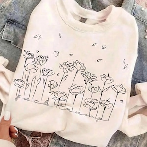 May include: A white ceramic mug with a black handle and the text "But First, Coffee" in a bold, black font. The mug is set against a blurred background, suggesting a cozy setting.