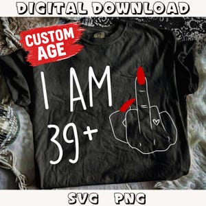 May include: Black t-shirt with white text that reads "I AM 39+". The graphic includes a hand with a red fingernail giving the middle finger and a small heart. The words "DIGITAL DOWNLOAD", "CUSTOM AGE", "SVG", and "PNG" are also visible.