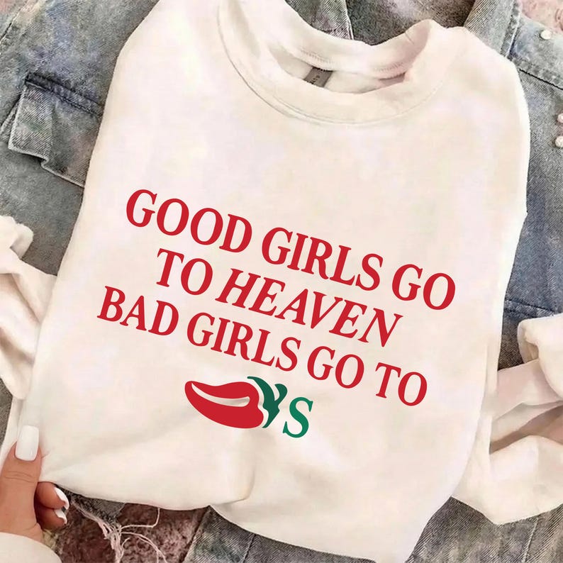 May include: White sweatshirt featuring the red text "GOOD GIRLS GO TO HEAVEN BAD GIRLS GO TO" and a red lip graphic with green accents. The sweatshirt is displayed on a denim jacket.