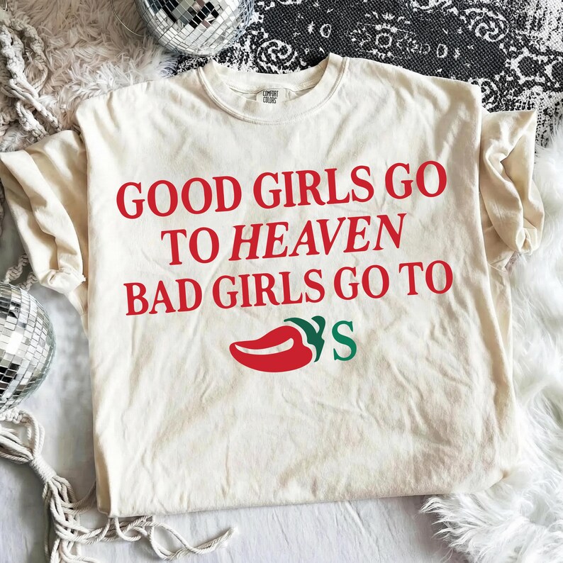 May include: Cream-coloured t-shirt with the text "GOOD GIRLS GO TO HEAVEN BAD GIRLS GO TO" in red, and a red chilli pepper graphic with green accents. The shirt is made of a soft material.