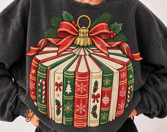 May include: A charcoal gray crewneck sweatshirt featuring a graphic of books arranged in a circular pattern to resemble a Christmas ornament. The design includes a red bow, green pine needles, and book spines decorated with candy canes and snowflakes.